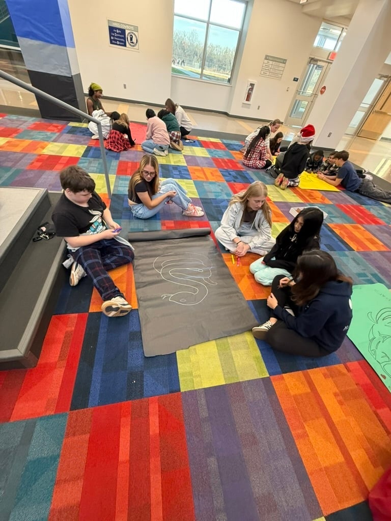 students-in-circle-sitting-on-colorful-carpet-drawing-on-poster