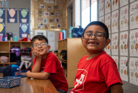 2 young boys smiling in a classroom