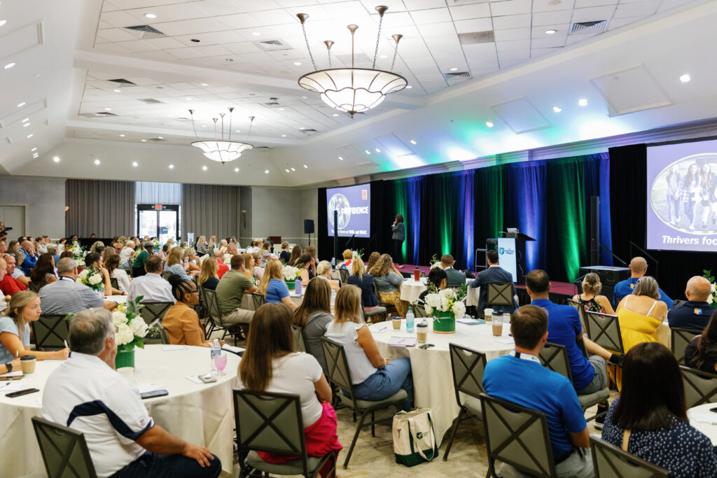An event hall full of people watching a talk at the national conference