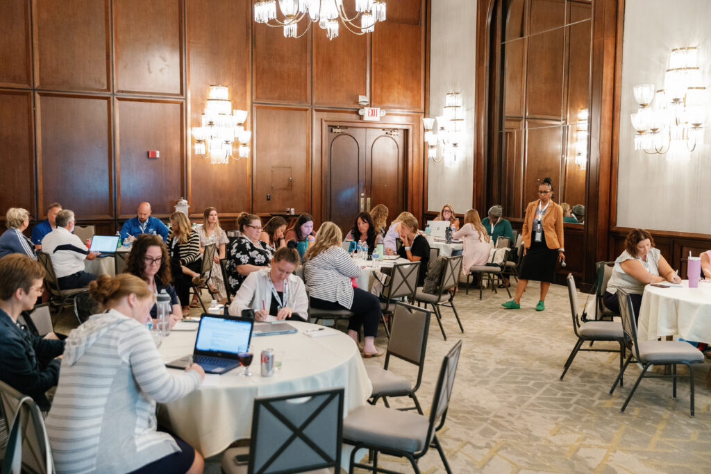 A large group of educators around tables in a hotel ballroom working at the P2 National Conference