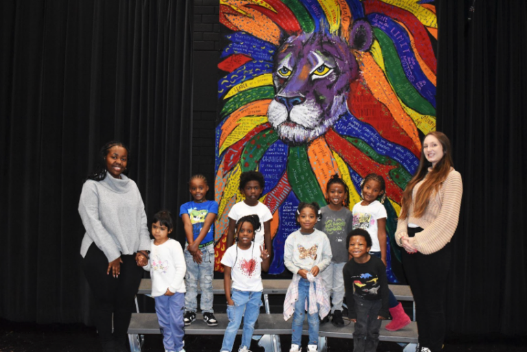Students and their teacher posing in front of a painting of a lion