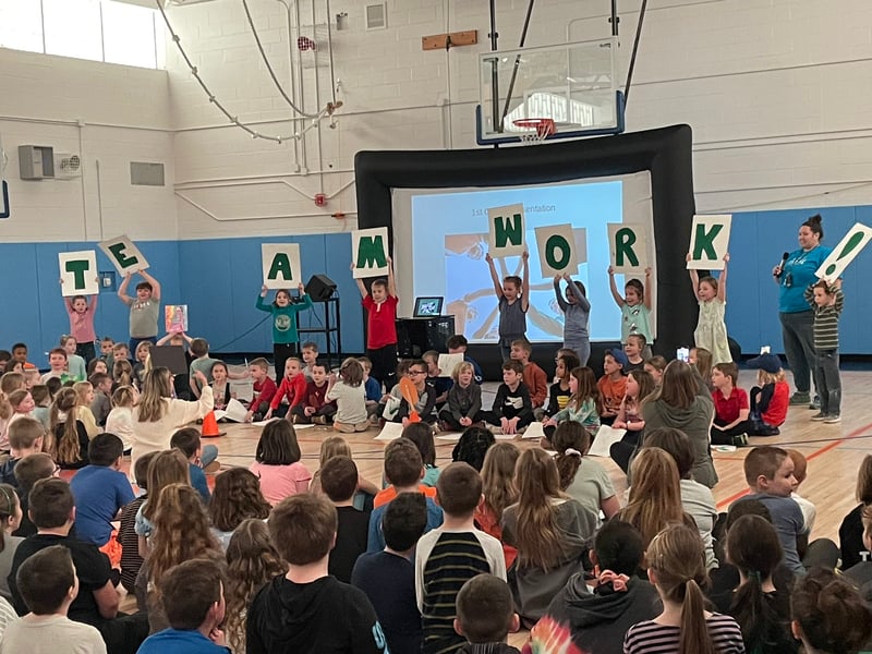 Kids hold up "Teamwork" signs at student assembly