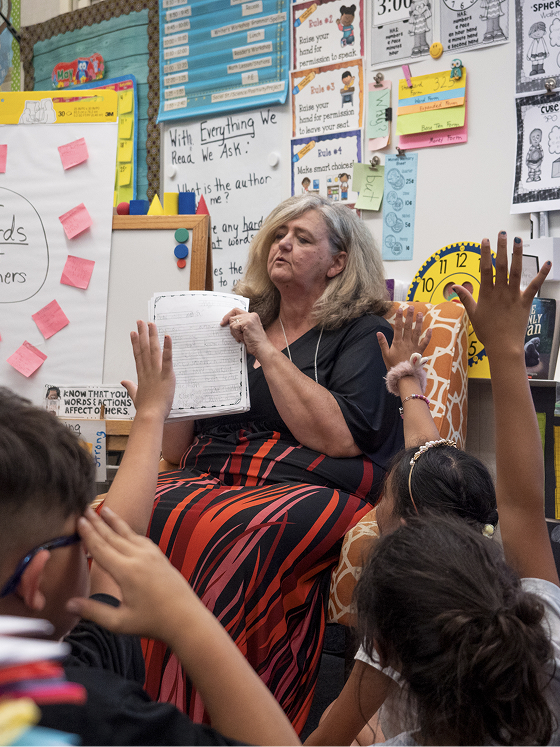 Students raise their hand, crowded around their teacher
