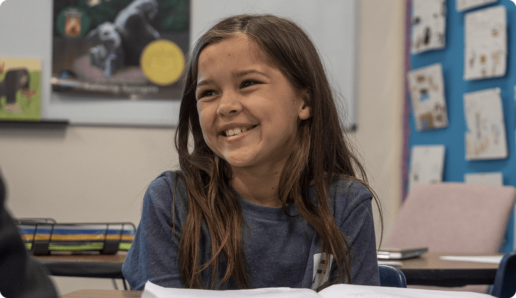 A smiling girl sits at her desk in a classroom