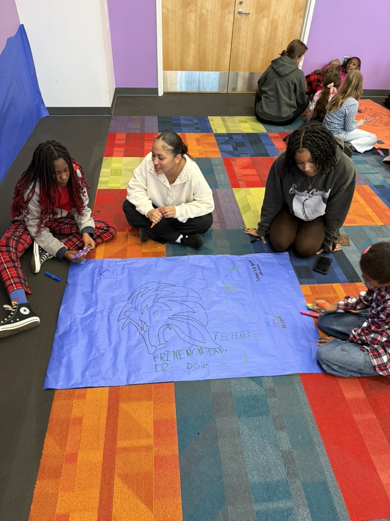 students-gathered-around-blue-poster-sitting-on-colorful-carpet
