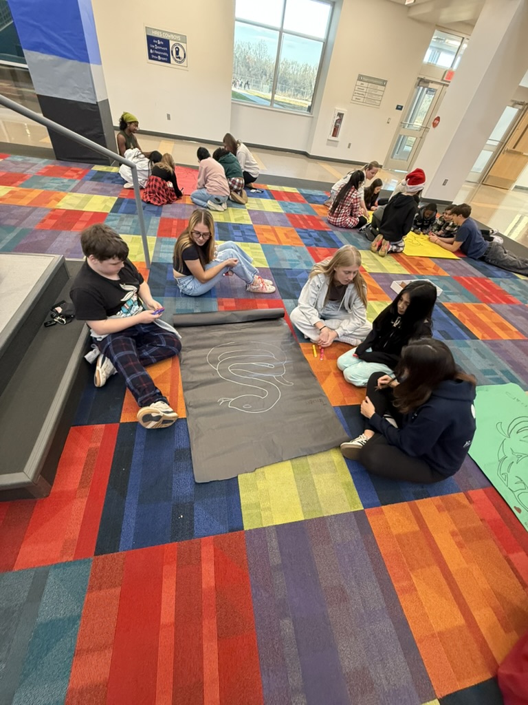 students-in-circle-sitting-on-colorful-carpet-drawing-on-poster