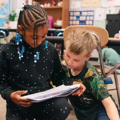 two-young-students-kneeling-looking-at-paper