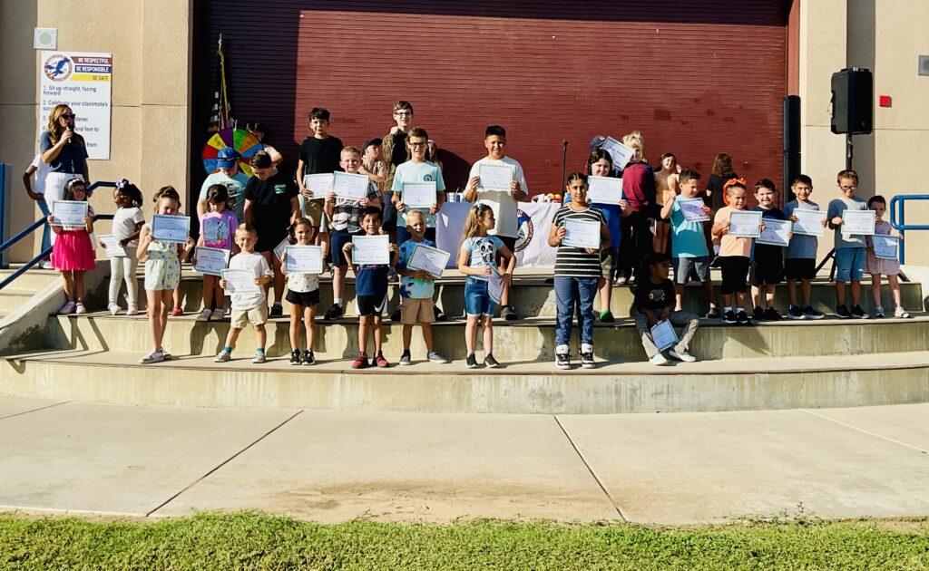 students-outside-on-school-front-yard-holding-certifcates-up