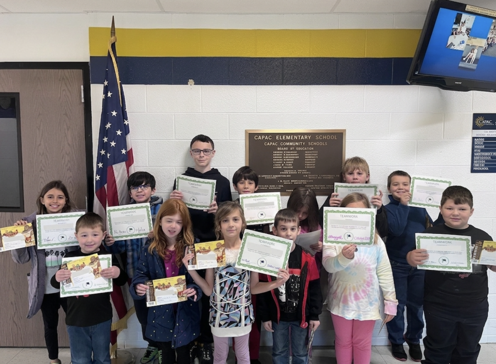 group-of-students-in-various-colored-clothing-holding-up-white-and-green-bordered-pieces-of-paper