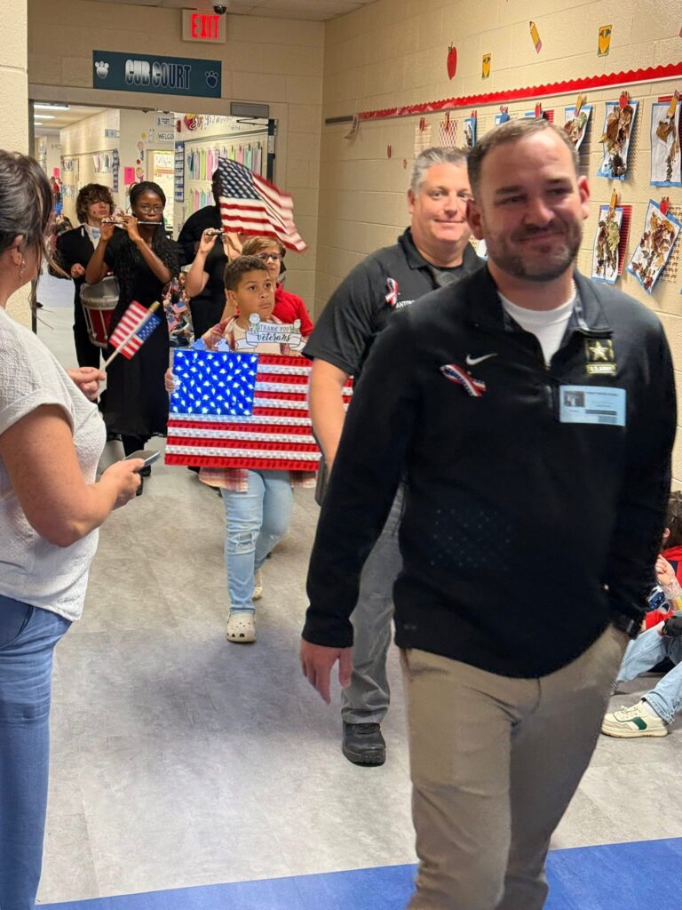 adults-walk-in-school-hallway-past-american-flags