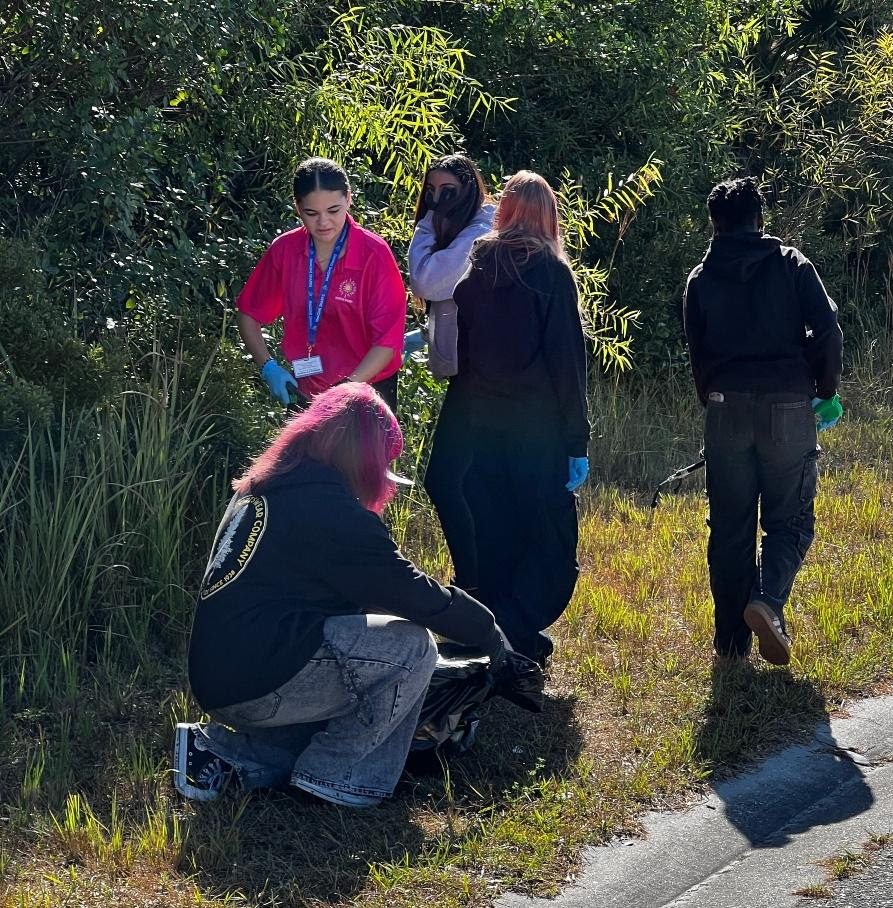 girl-with-pink-hair-bending-down-to-pick-up-trash-in-the-grass-near-other-students