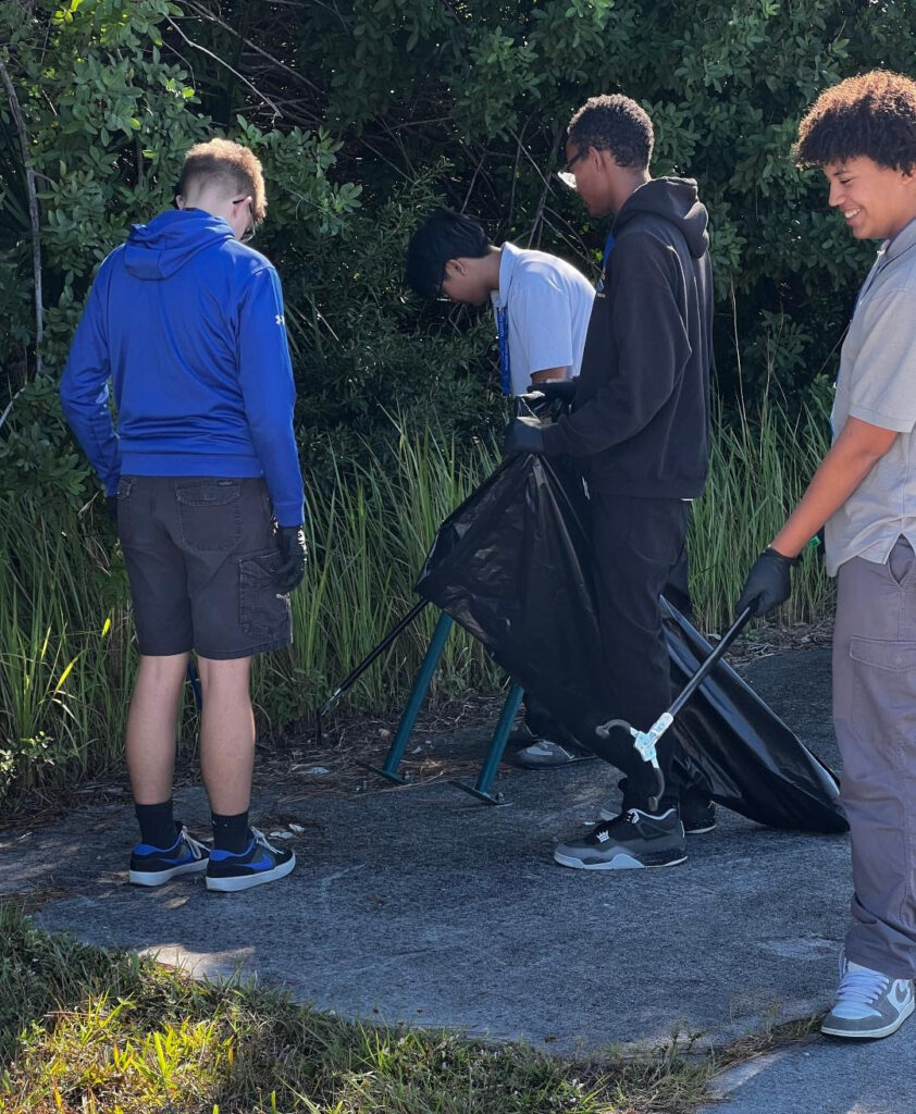 group-of-male-students-picking-up-trash-and-putting-into-trash-bag-outside
